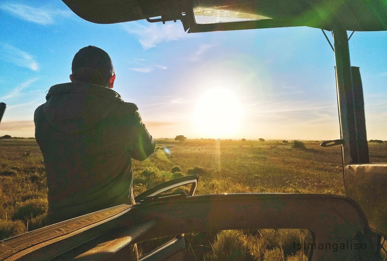 A guide watching sunrise over open grassland from an open-sided game-drive vehicle