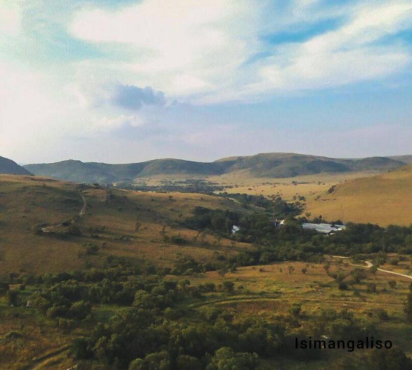 A rolling grassland valley with farm buildings and hills on the horizon