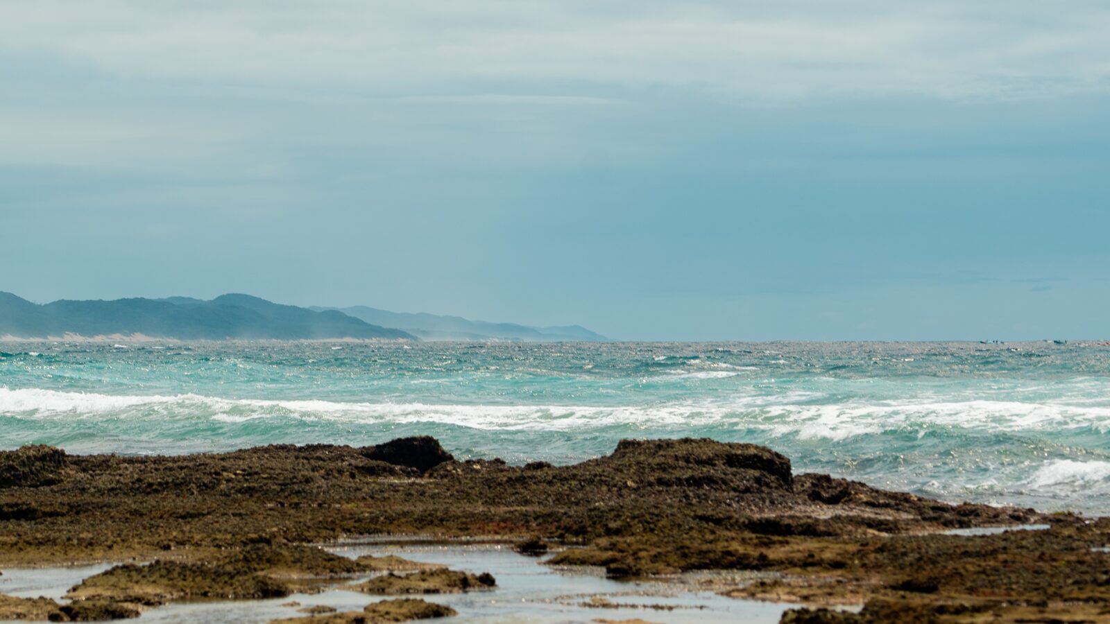 A rocky shore with surf breaking and a dune coastline stretching away
